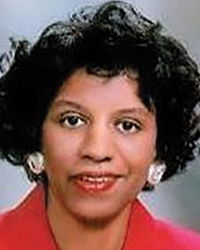 A black woman with short dark curly hair smiles at the camera. 