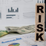 "RISK" spelled out in blocks on top of printed graphs, charts, and money.