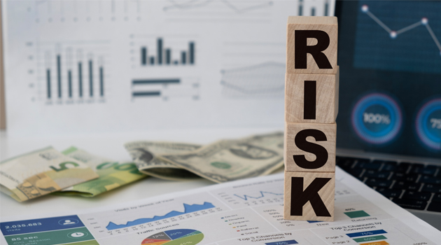 "RISK" spelled out in blocks on top of printed graphs, charts, and money.