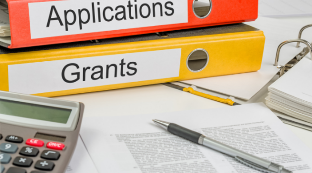 Binders labeled "applications" and "Grants" with writing tools in the foreground