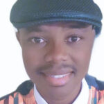 Timothy Boakye smiles at the camera in a black page boy hat, a kente-patterned vest and bowtie, and a white shirt.