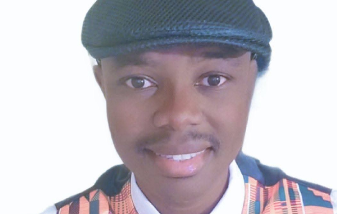 Timothy Boakye smiles at the camera in a black page boy hat, a kente-patterned vest and bowtie, and a white shirt.